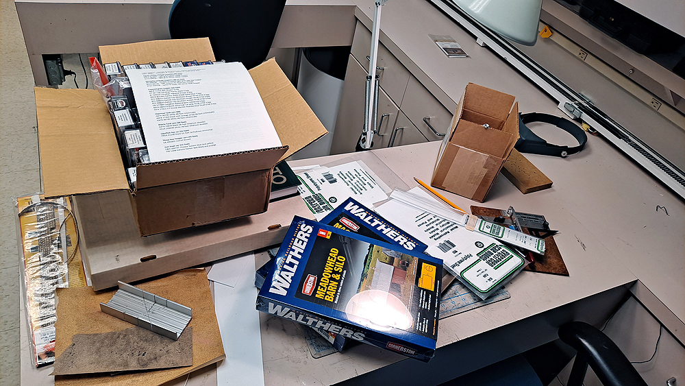 Freight car boxes, model kits, tools, and scratchbuilding supplies cover a workbench.