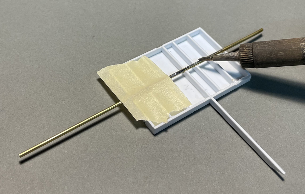 Photo showing piece of brass rod taped to styrene being heated with soldering iron. 