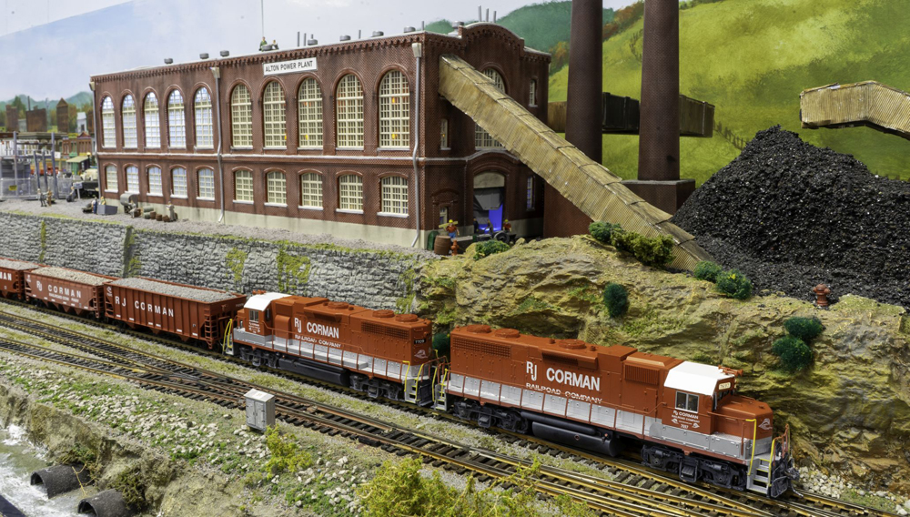 A model railroad layout with a train in the foreground and a large warehouse in the background