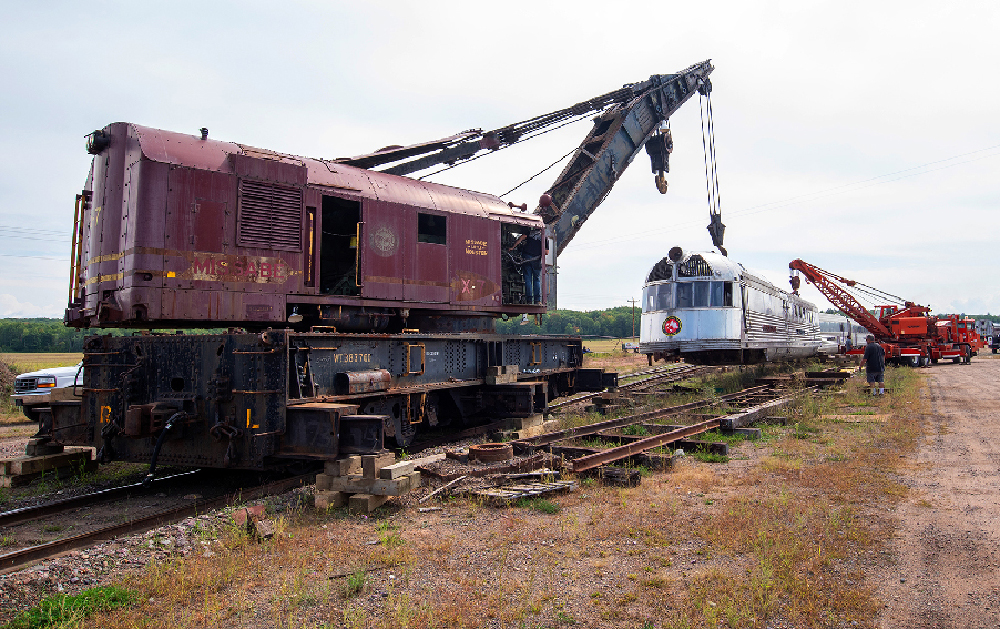 Two cranes lifting a shovel-nosed locomotive. Wisconsin Great Northern places 'Mark Twain Zephyr' back on its trucks
