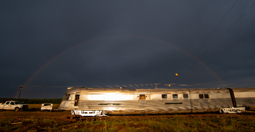 Silver shovel-nosed train under a dark sky with a rainbow. Wisconsin Great Northern places 'Mark Twain Zephyr' back on its trucks