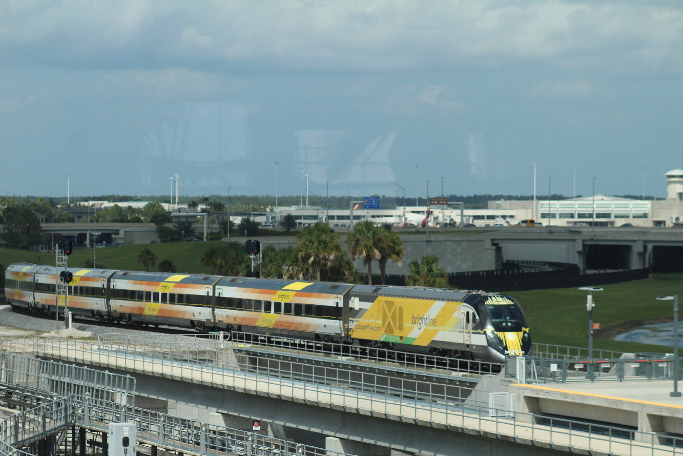 Yellow, white, and black passenger train arriving at station. Brightline inaugurates Orlando service.