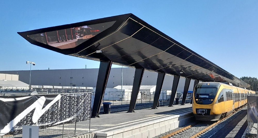 Yellow train standing at the platform of a new modern passenger station. Tesla buys German railway line, plans passenger trains.