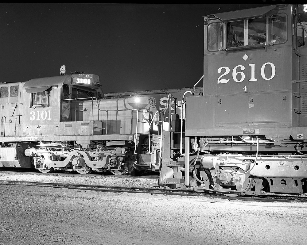 A time-exposure nighttime photo shows the cab of a switch engine in the foreground and the cab of an Alco RSD15 road switcher in the background