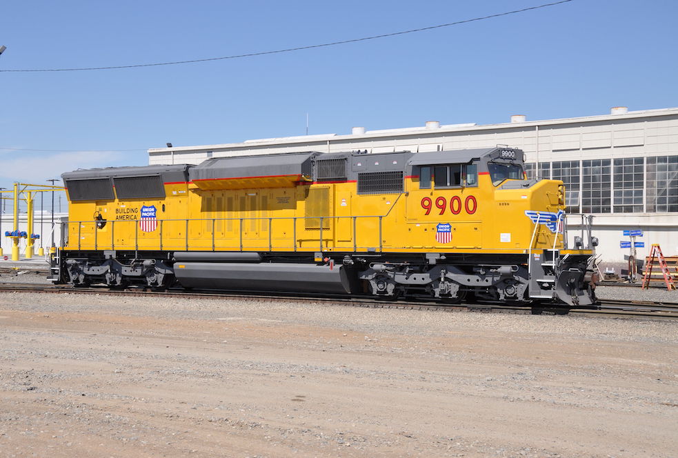 The right side of a yellow locomotive beside a white building