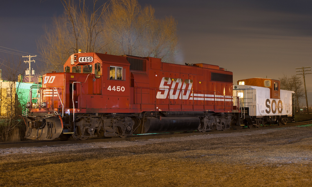 A night view of a red diesel locomotive with large white lettering on the side reading Soo