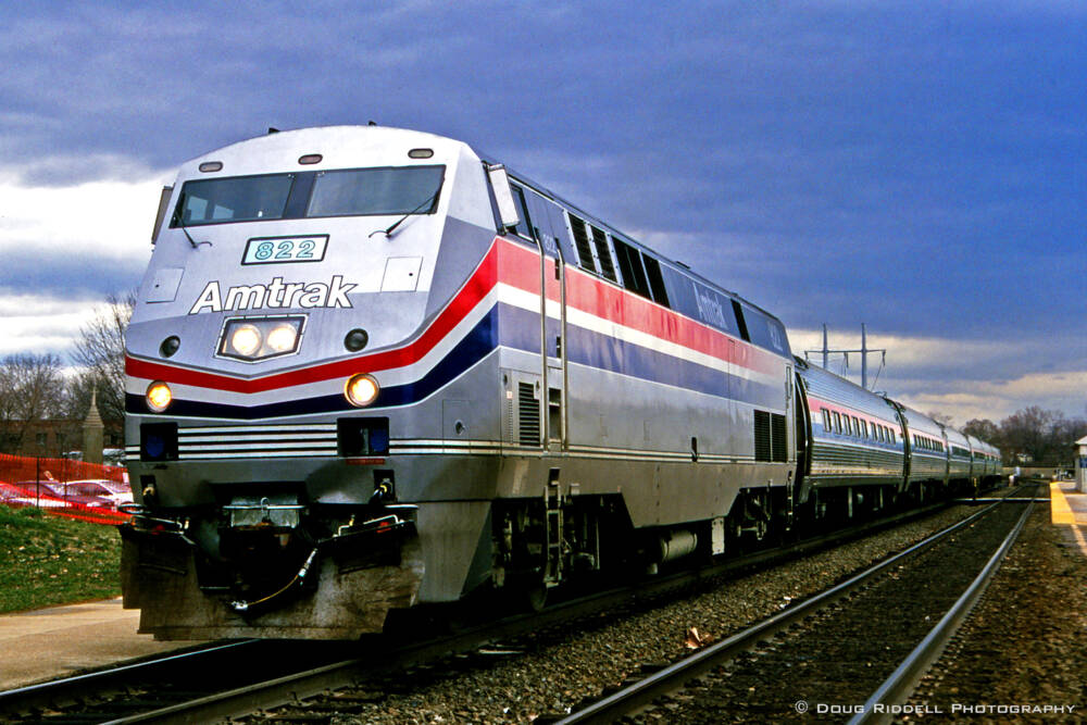 A silver Amtrak locomotive at the head of passenger cars under a dark stormy sky