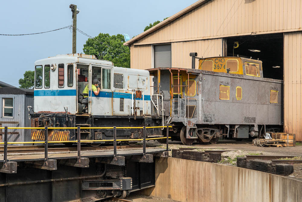 Diesel-powered switcher tows a caboose onto a turntable.