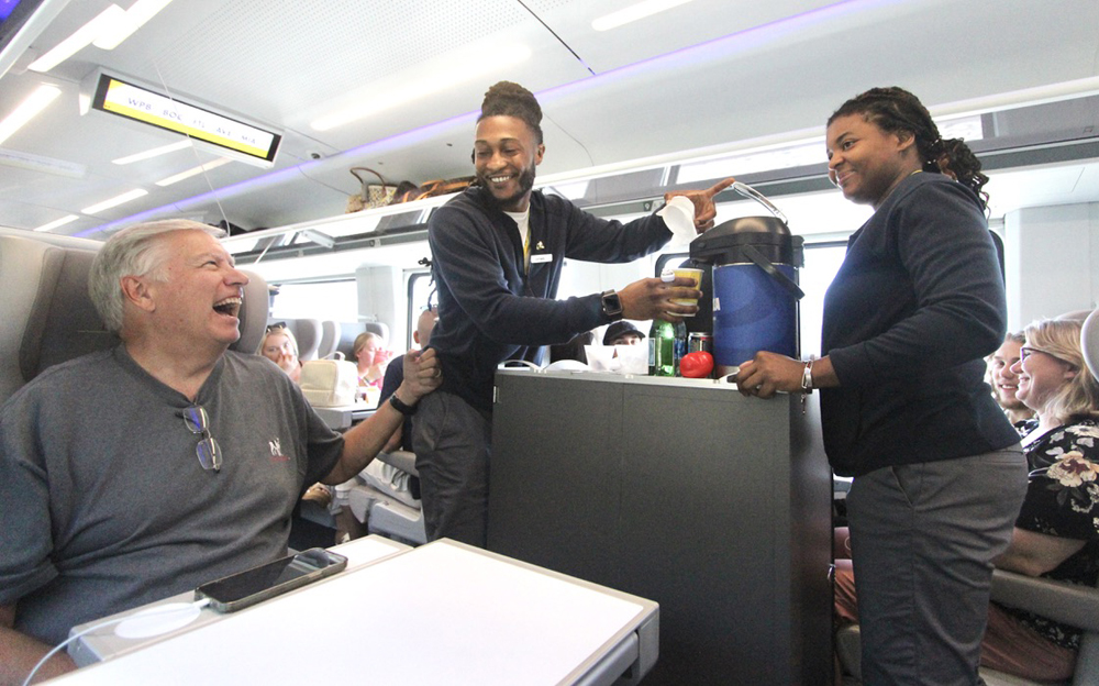 Man in seat jokes with two women with serving cart on train