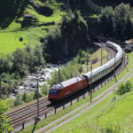 Passenger train with electric locomotive rounds curve after exiting tunnel