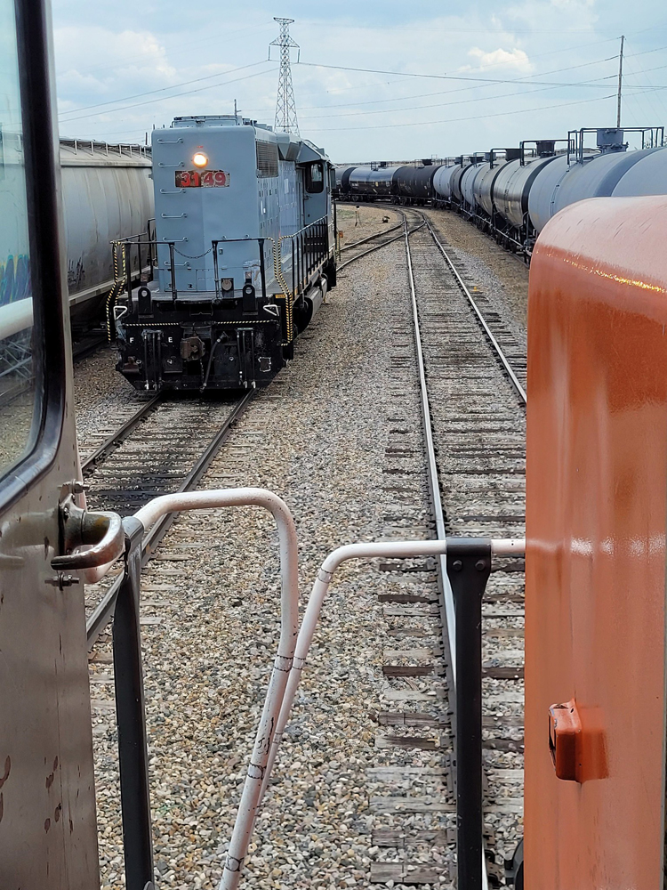 View of gray locomotive and freight cars from on board another locomotive