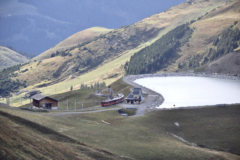 Train passes station next to lake as seen from altitude