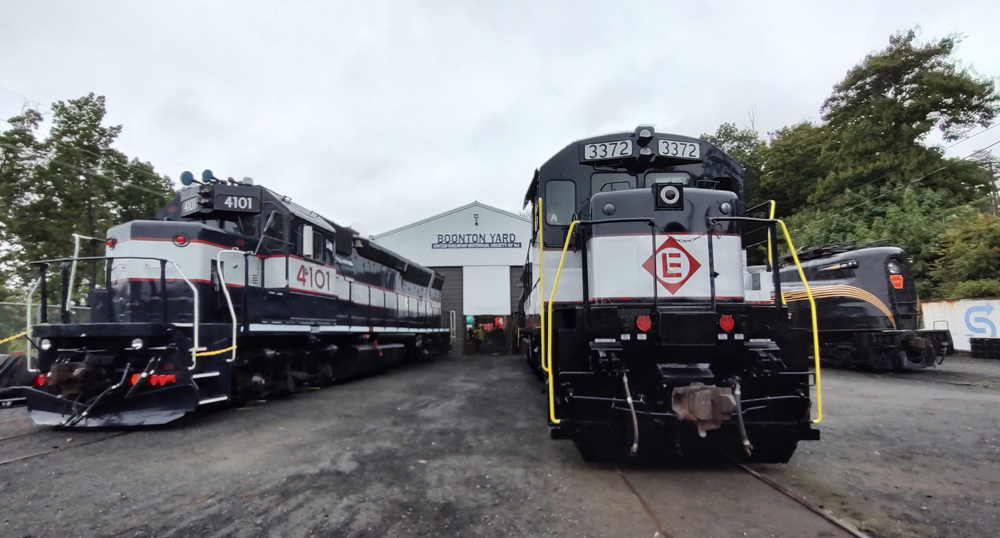 Dark blue diesel locomotives with white center stripe outside shop building