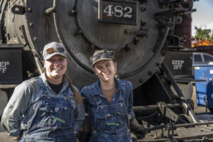 Two women standing at front of steam locomotive