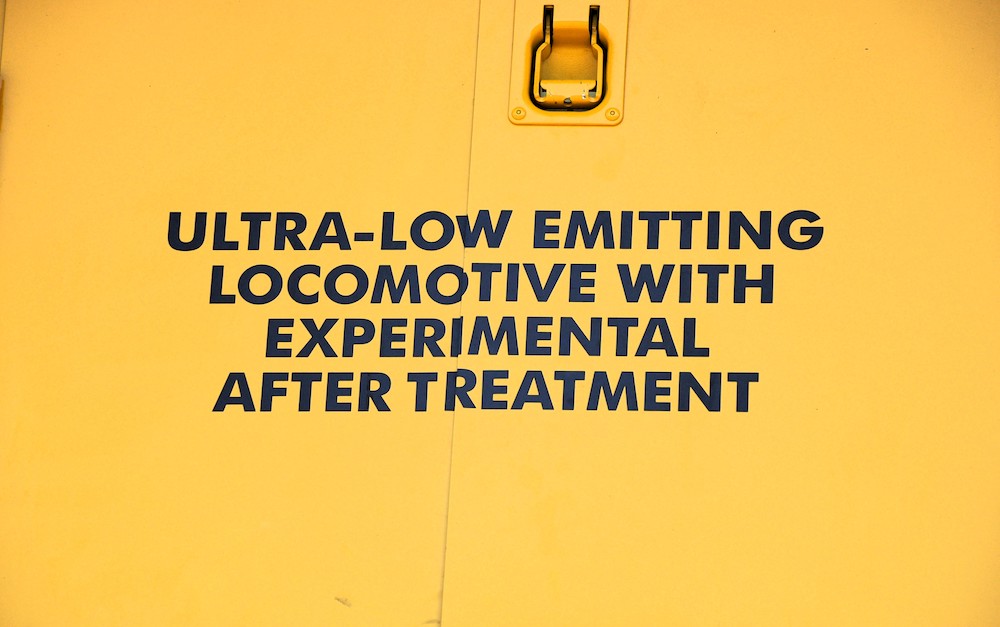 A stenciled message in black lettering on the side of a yellow locomotive