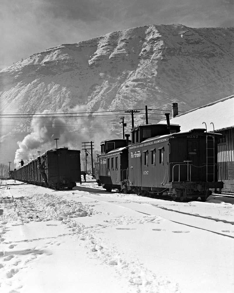 Railroad cabooses in snow beneath mountains