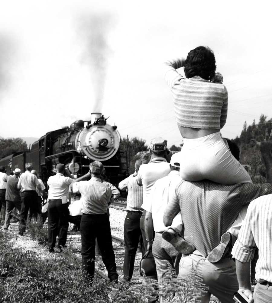 Woman sits on man's shoulders to view steam locomotive