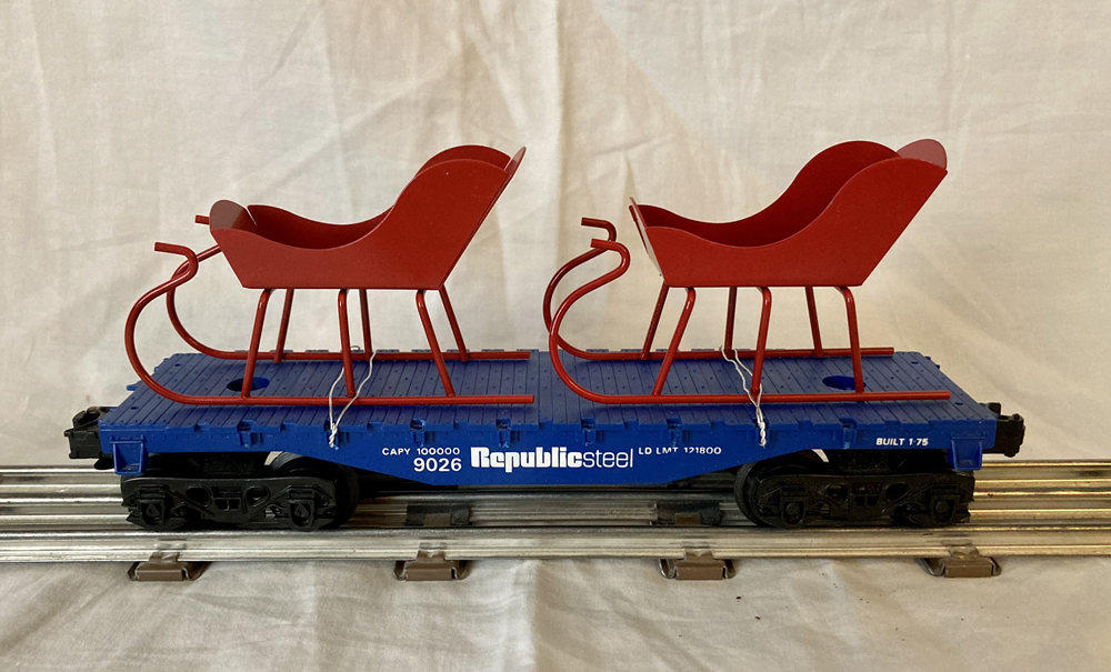 blue model flatcar with two red sleighs on top