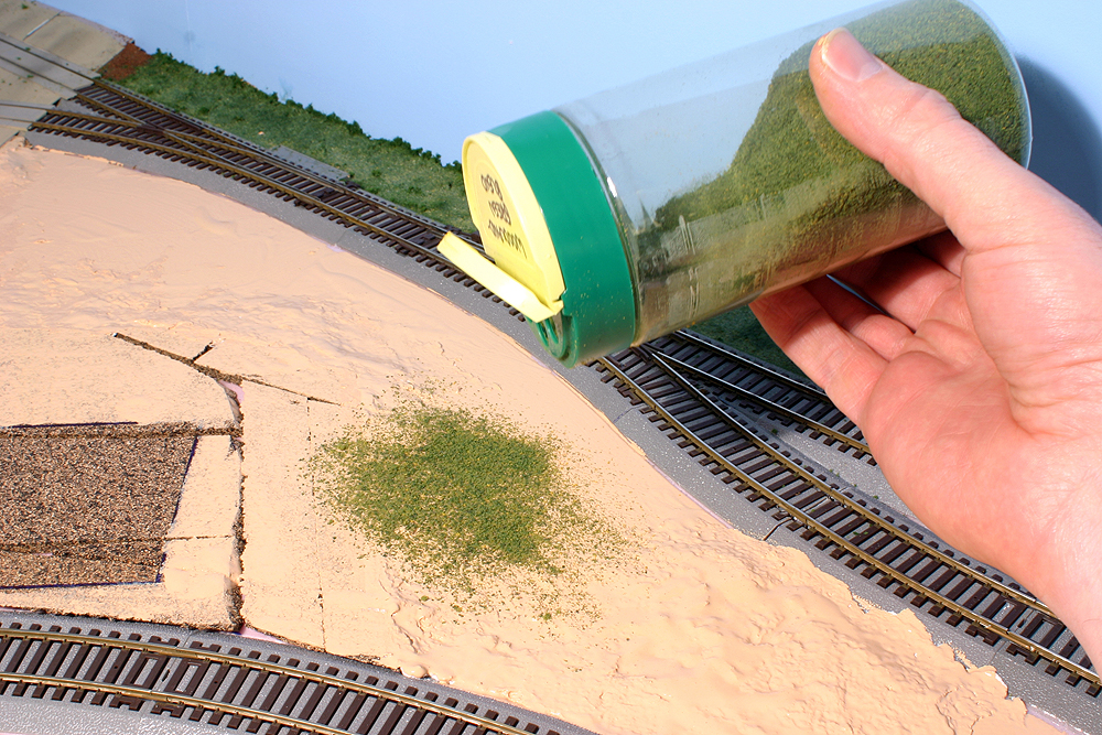 Green ground foam is sprinkled onto a tan layout surface
