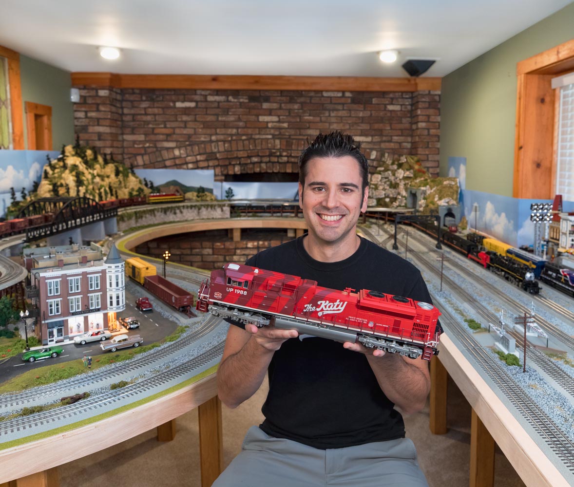 Man smiles while holding red model train locomotive