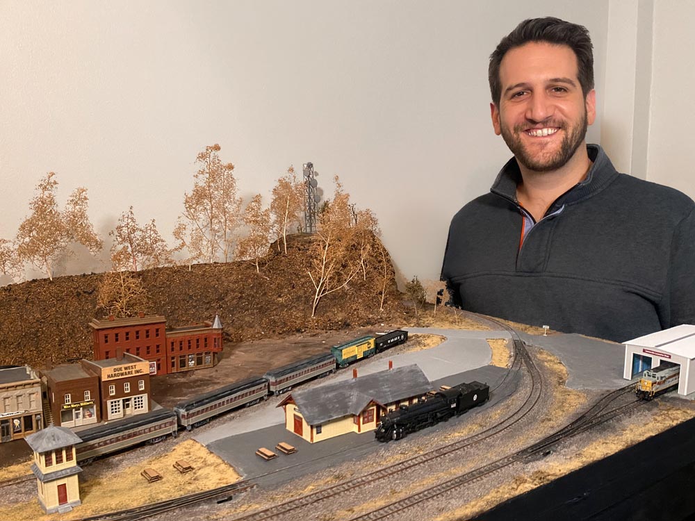 Man in sweater smiles next to train layout