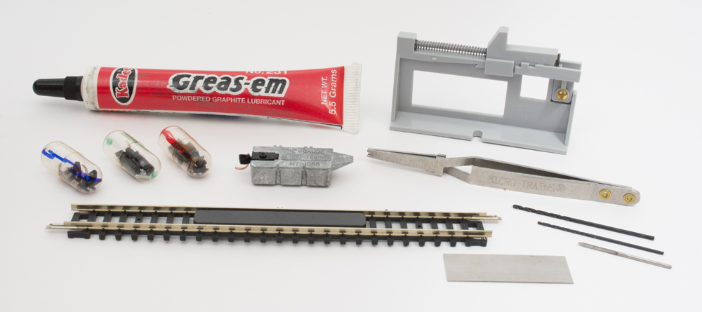 Color photo showing section of N scale track, coupler height gauge, tube of graphite, and assorted tools.
