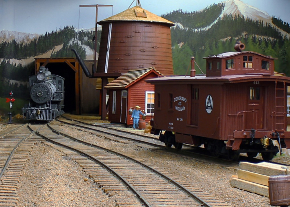black model steam engine next to structure and boxcar on model railroad