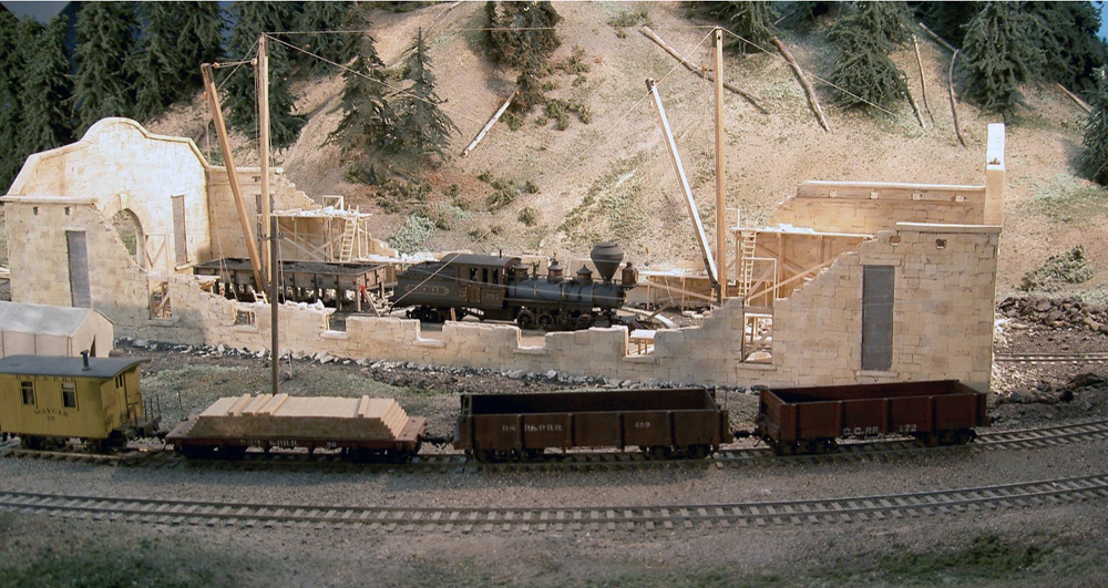 black model engine on turntable with partially built structure and train cars on track in front