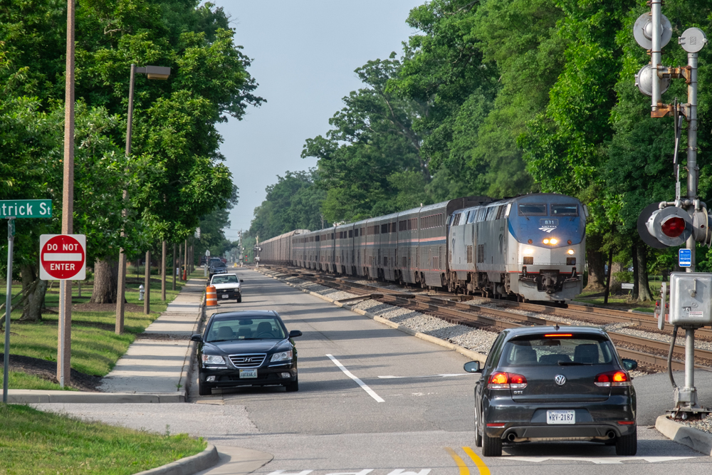long blue and white Amtrak train in middle of road on tracks