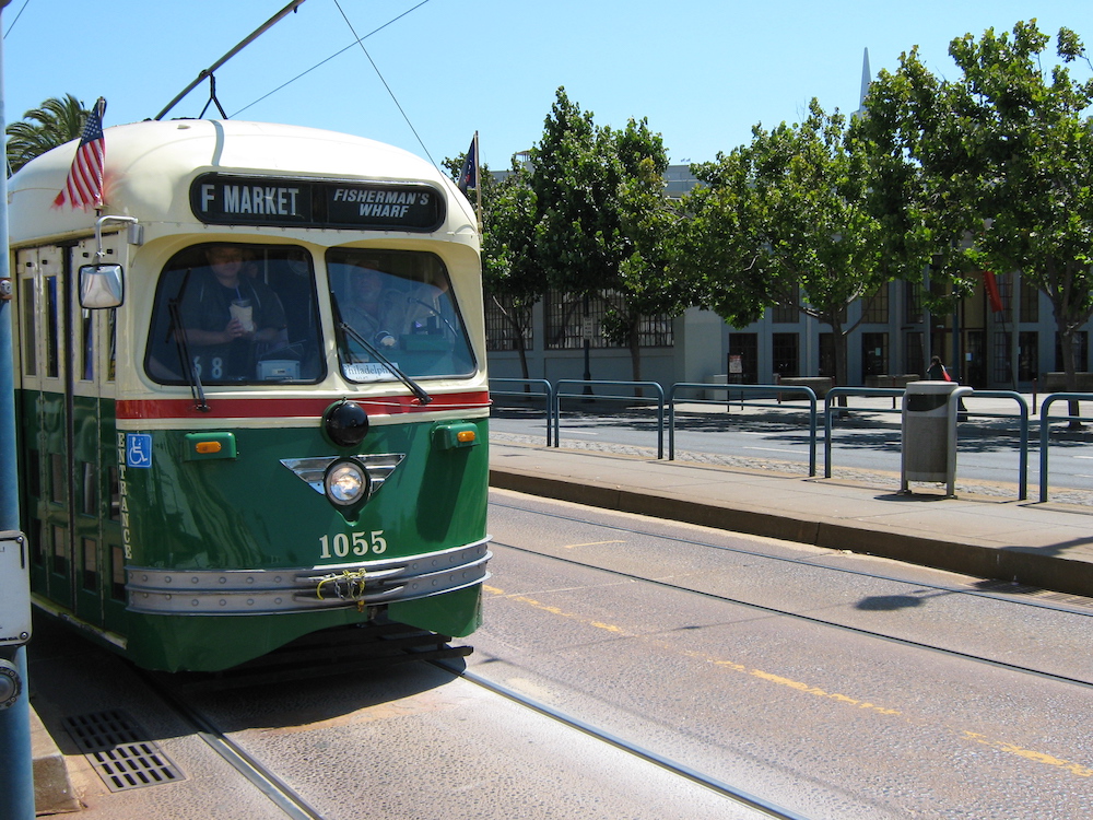 With a tree-lined street in the background a green and cream streetcar passes by under a clear sky