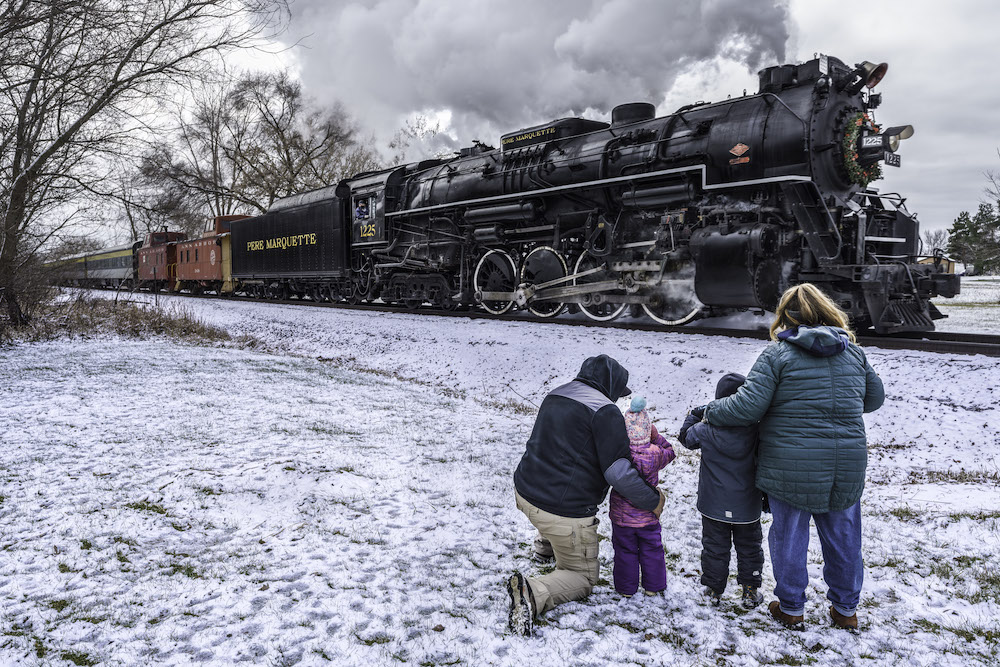The family watches a steam-powered train go by during the winter.