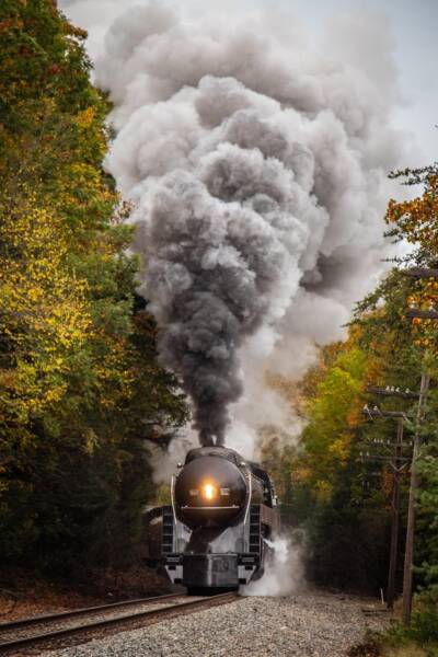Streamlined steam locomotive running through the fall foliage.