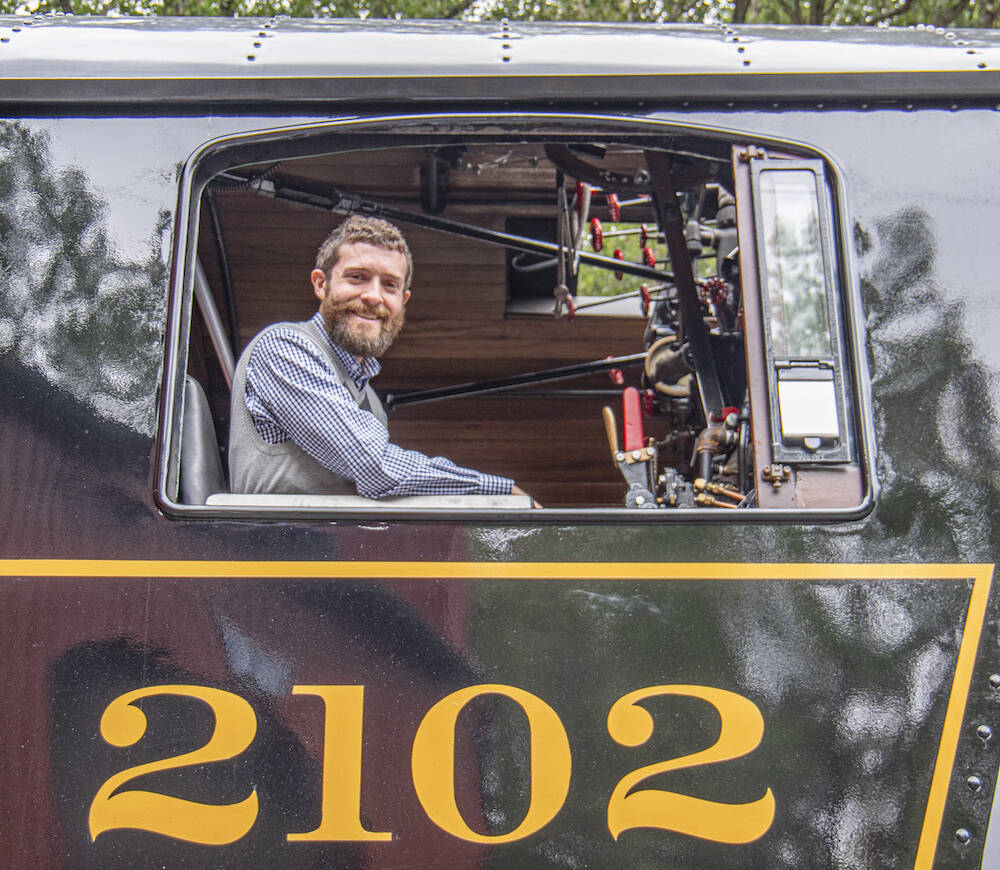 Young individual posing in the cab of a steam locomotive.