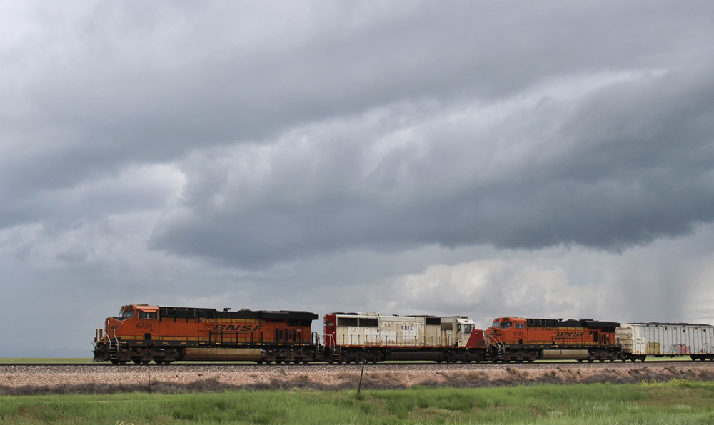 Freight train with three locomotives under dark clouds