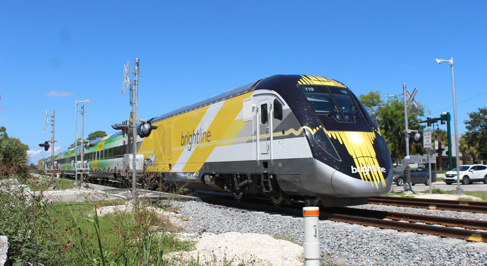 Yellow and white locomotive leading train through grade crossing
