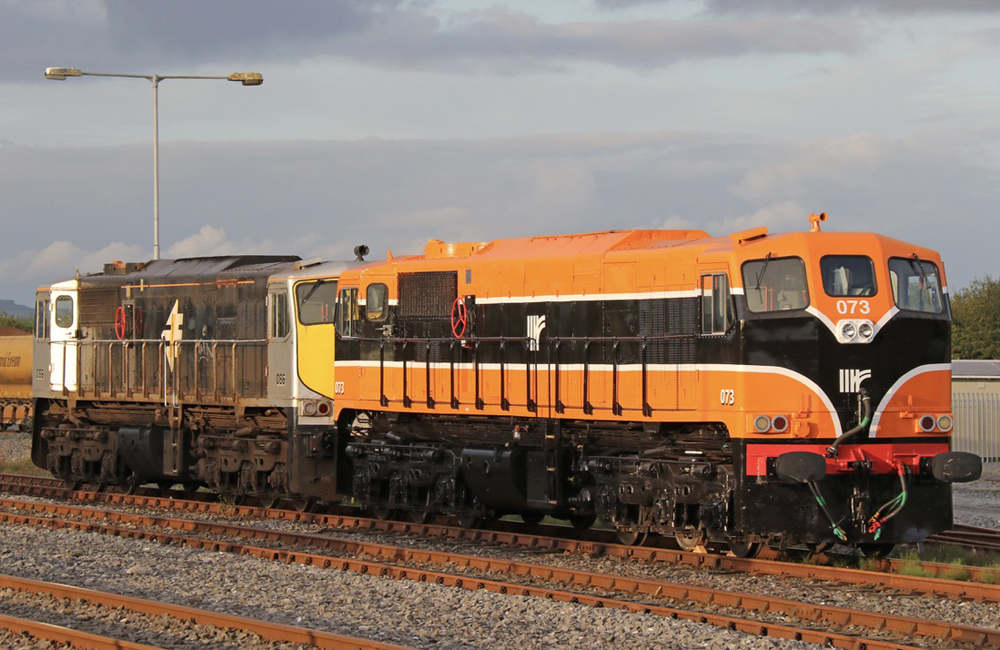 Orange and black double-cab locomotive coupled to similar locomotive with gray paint