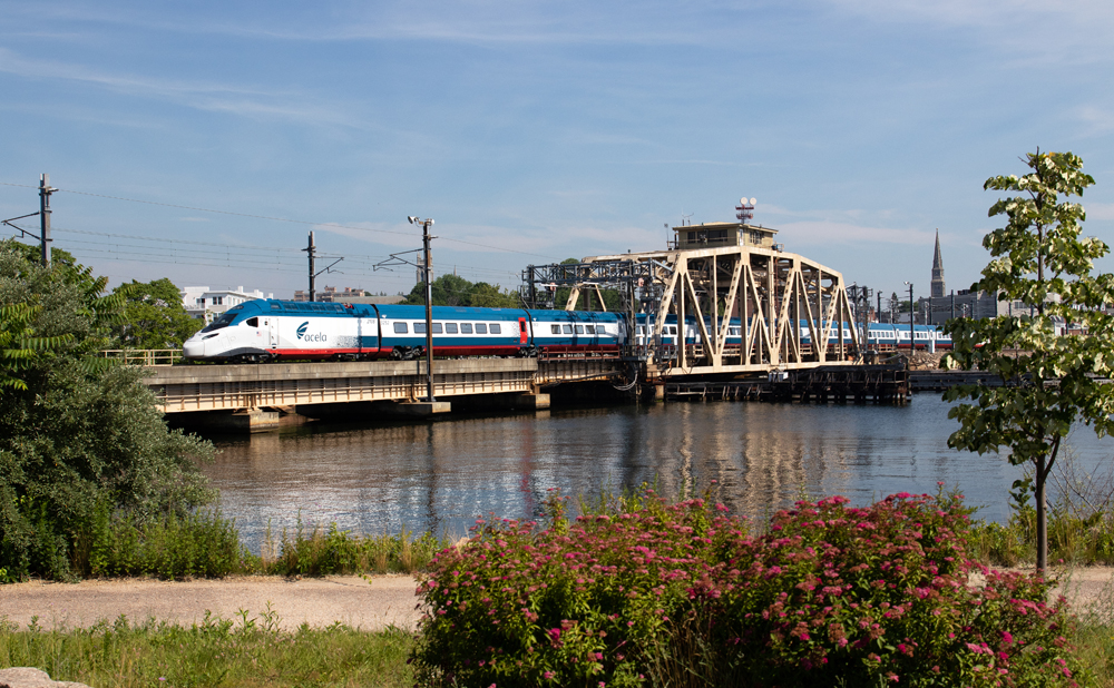 Streamlined blue and white high-speed passenger train crosses bridge