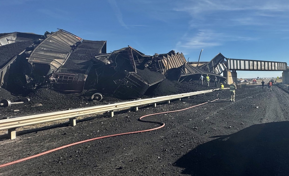 Derailed coal hoppers piled up on highway, with coal on roadway. Colorado rail safety bill
