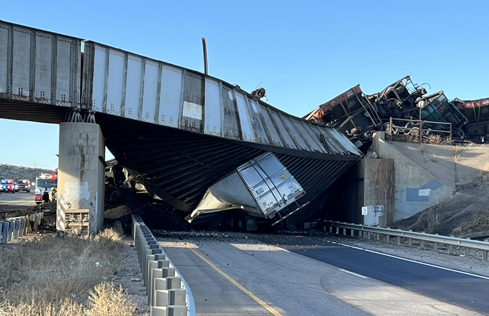 Truck pinned under collapsed freeway bridge beneath derailment