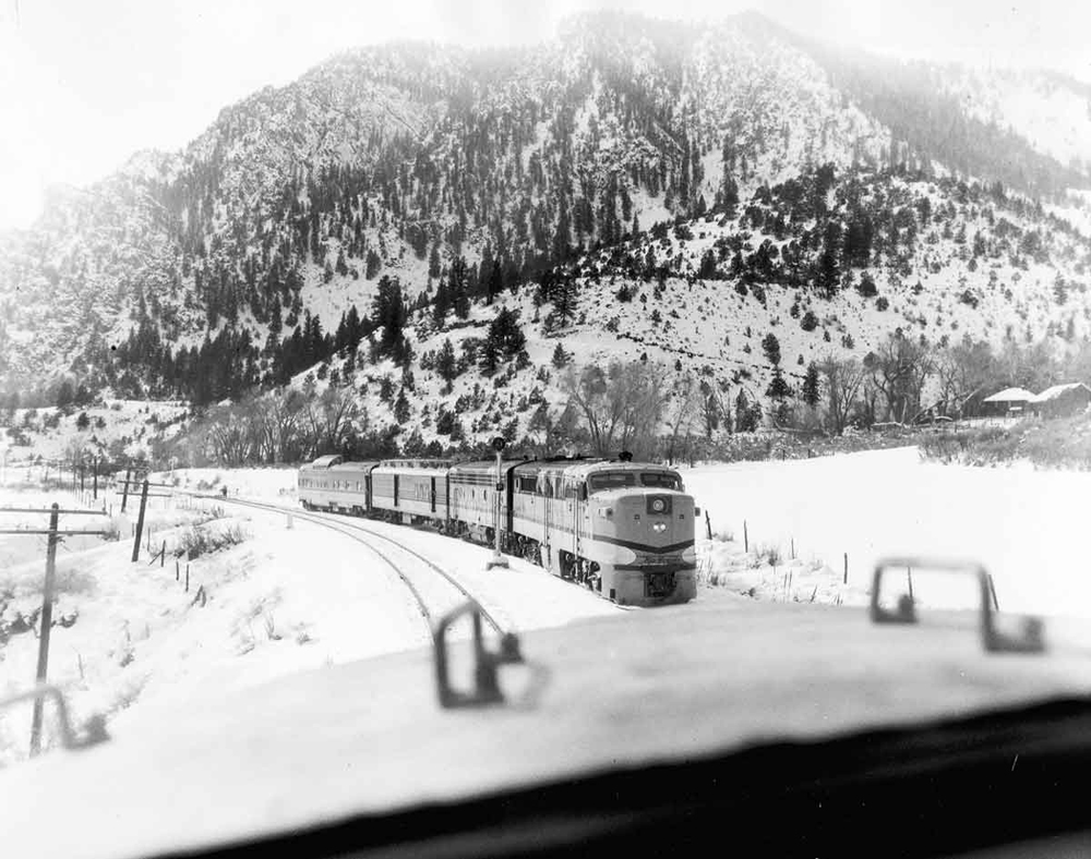 Black and white photo of passenger trains meeting in snow-covered mountain area