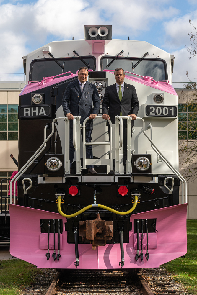 Two men posing on front platform of pink, white, and black locomotive