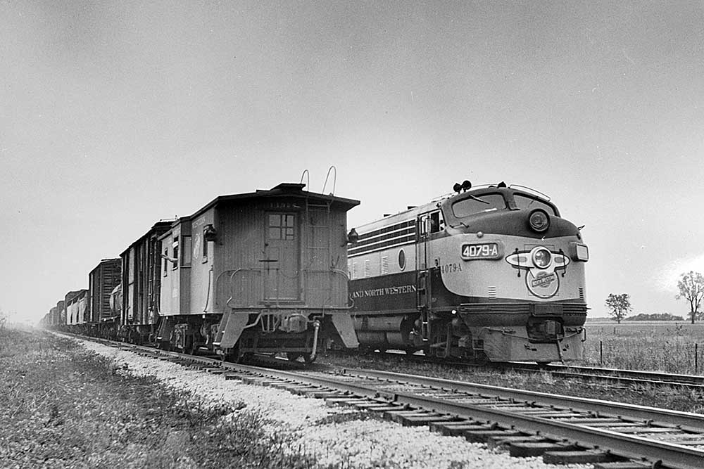 Streamlined Chicago & North Western diesel locomotive passing wooden caboose