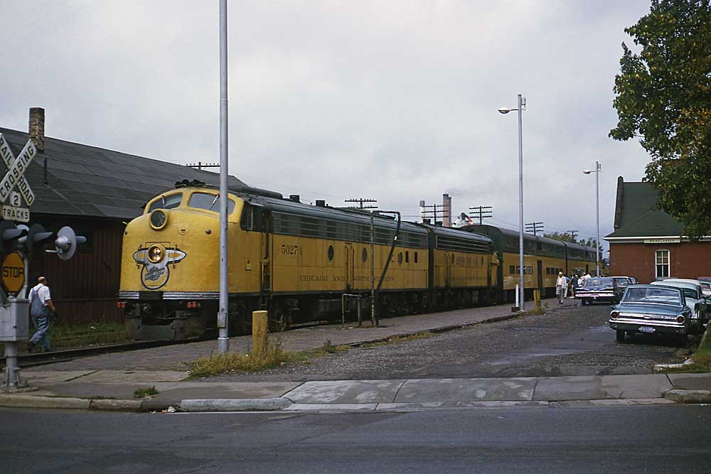 Yellow-and-green passenger train at station by grade crossing