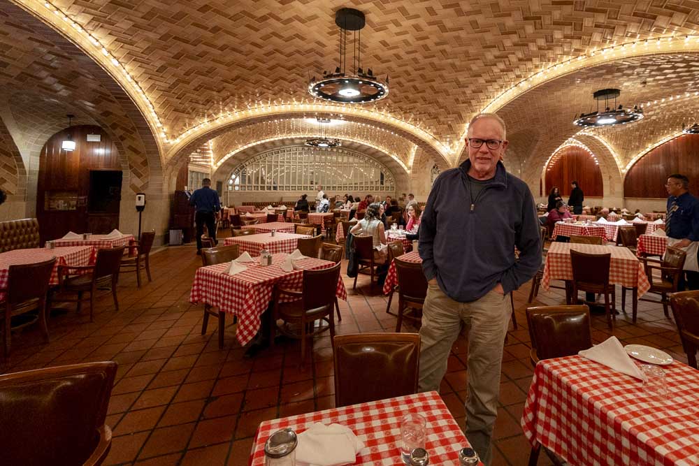Man stands in restaurant with no windows and red-and-white checked tablecloths
