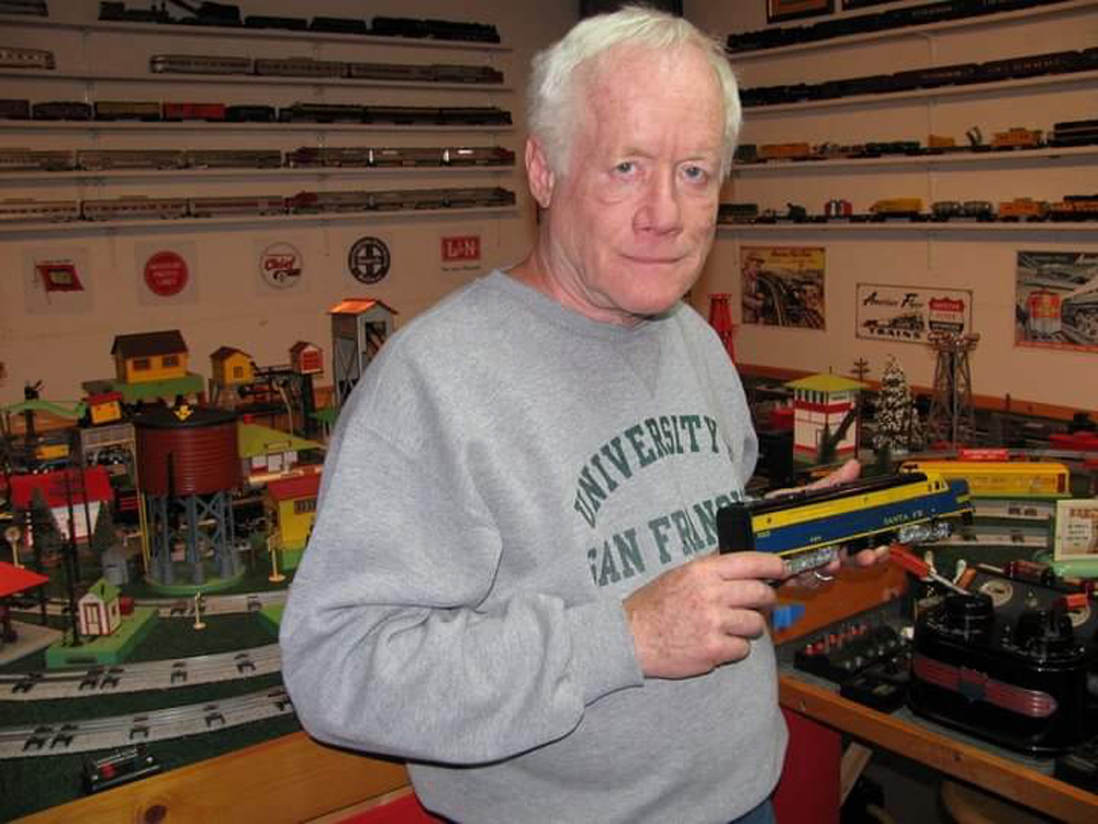 man holding toy train next to layout