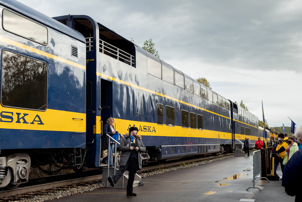 A railroad employee stands beshide a blue and yello passenger train