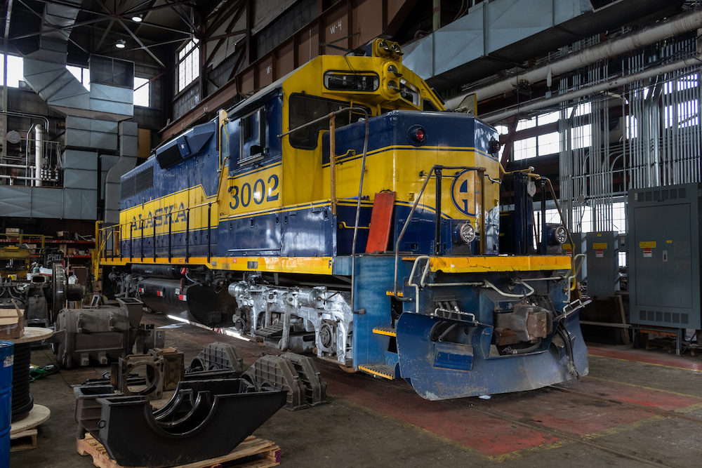 A blue and white locomotive undergoes repairs in a large shop building