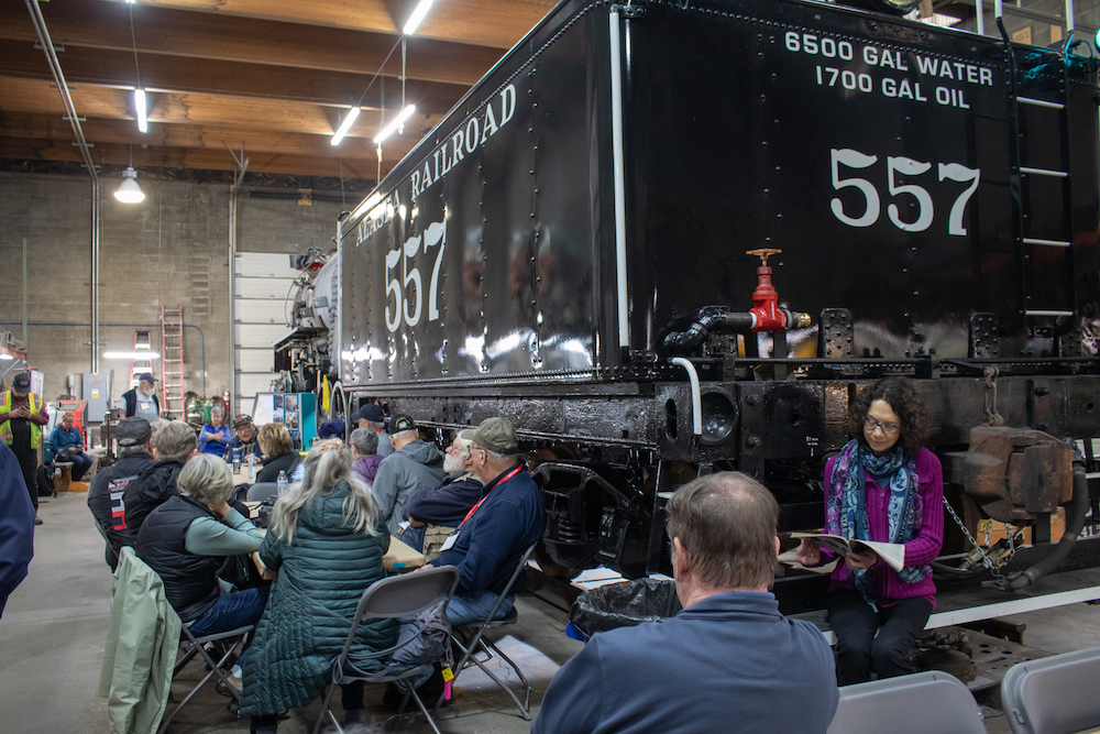 People sit at tables surrounding the large black tender of a steam locomotive