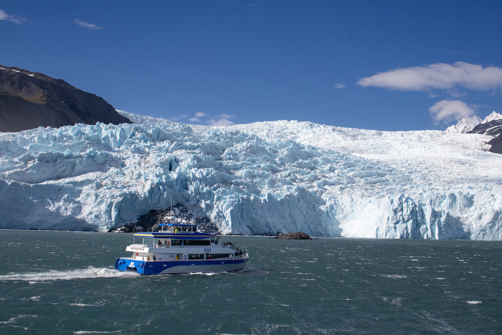 A white and blue tour boat passes in front of a glacier