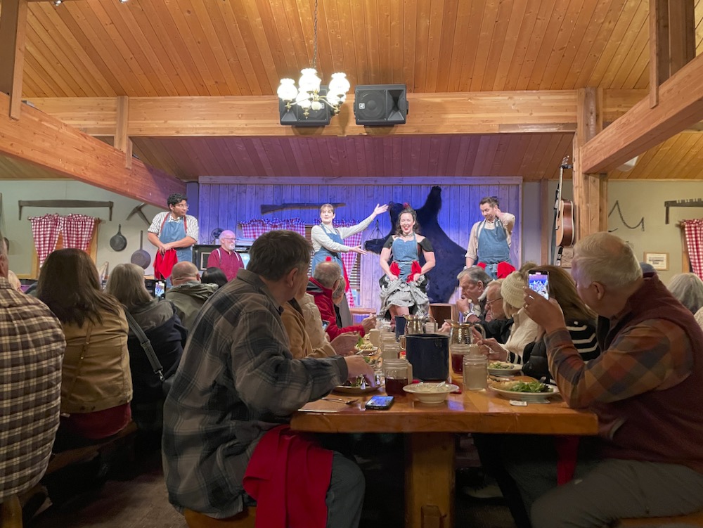 People at wood tables tables watch a stage show